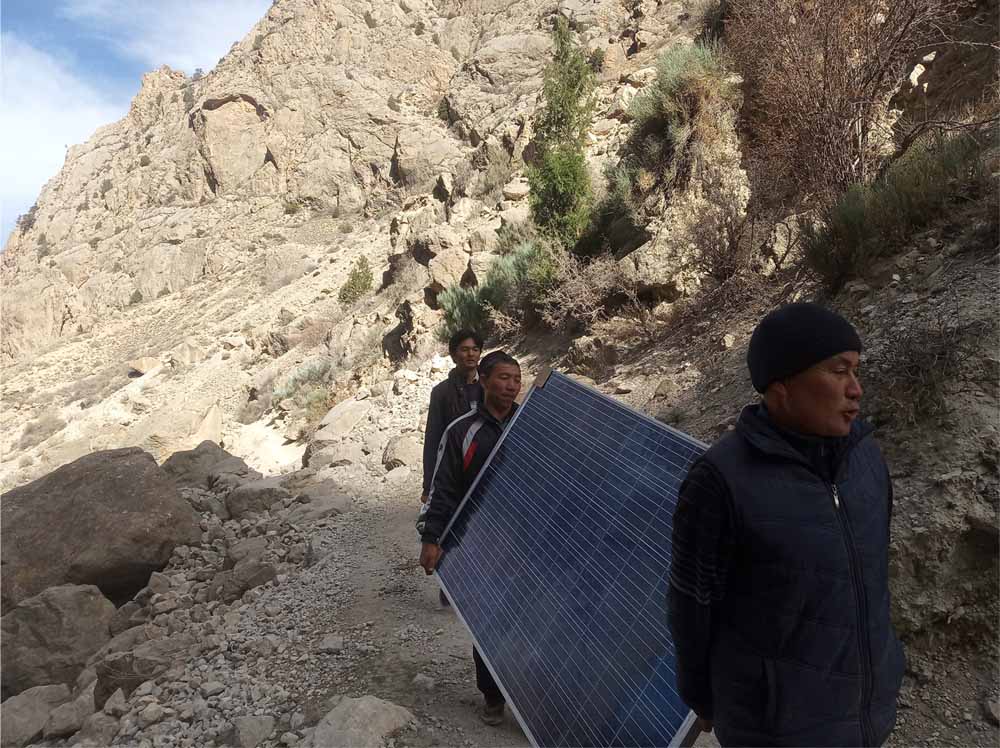 Two people carry a solar panel up a path