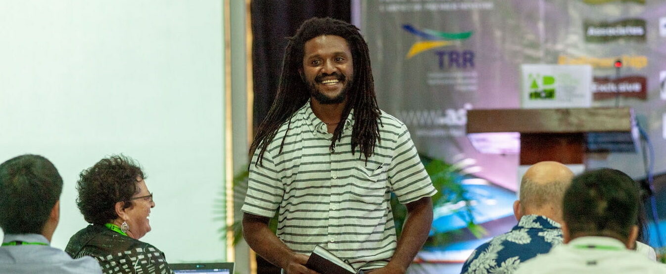 Man with long hair smiling while walking between people sitting at an event