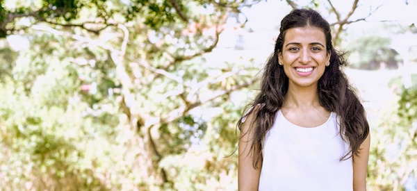 A woman in a white shirt smiling in front of trees.