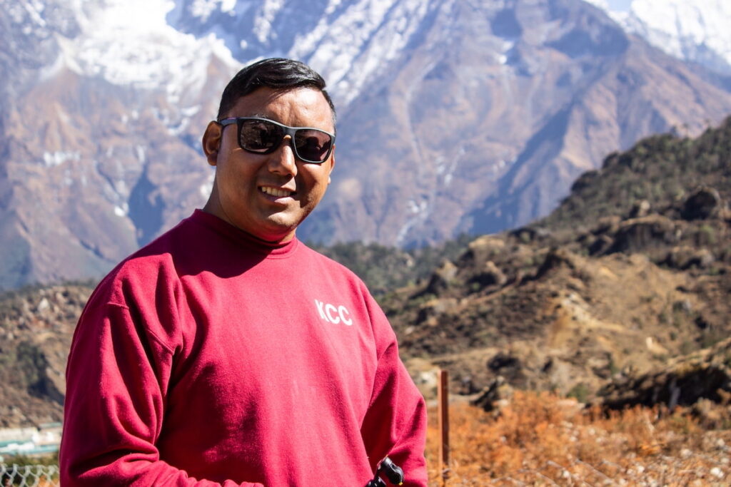 un impresionante paisaje montañoso, con picos nevados y un hombre sonriendo a la cámara