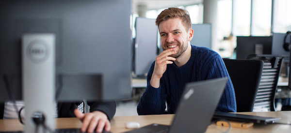 un homme à son bureau devant son ordinateur, souriant