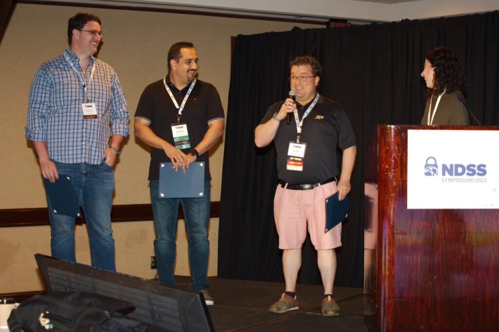 Photo of the three authors being presented with the award for 2022 Distinguished Paper on stage.