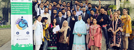 A group shot of men and women standing in front of a poster about accessibility