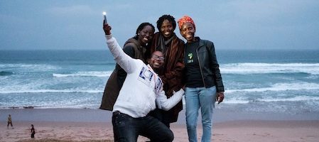 three women standing and a man holding a phone