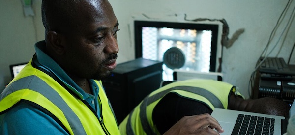 Un homme portant un gilet de sécurité est concentré sur son ordinateur portable