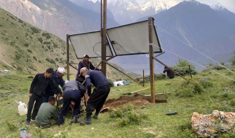 A group of people set up equipment with mountains in the background.