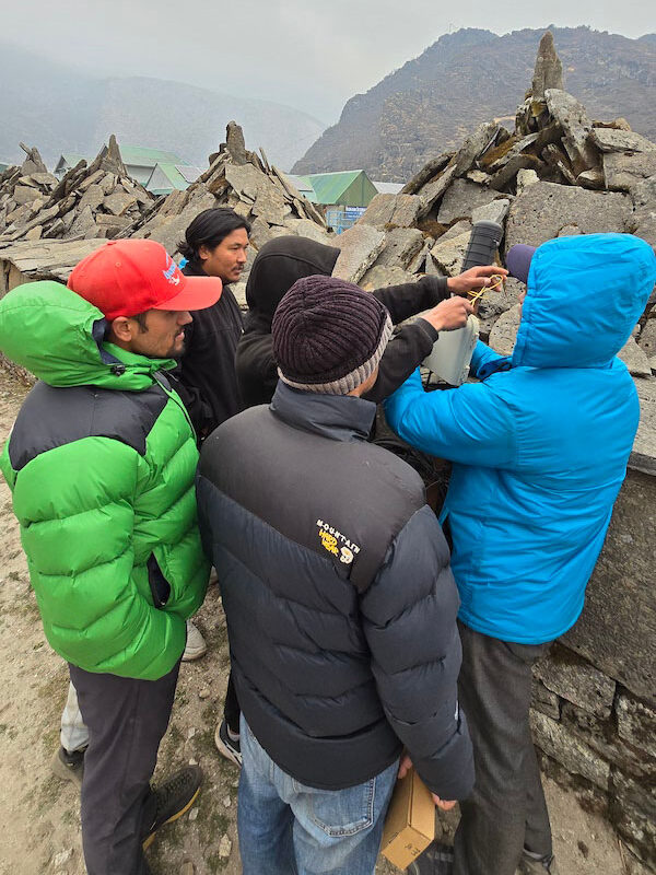 Students huddle around a piece of Internet infrastructure. There are stone piles behind them.