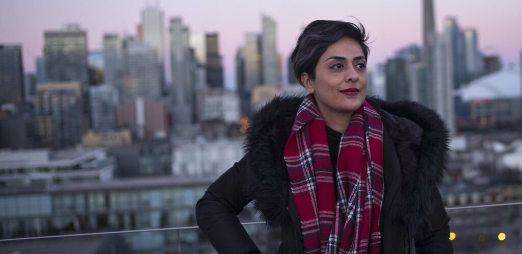 a young woman with short black hair standing on a balcony with a view of the city