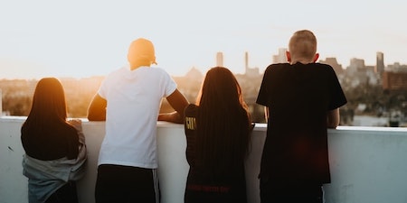 Deux filles et deux garçons debout sur le toit et regardant une ville au loin