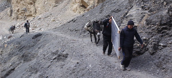 People carry a solar panel uphill.